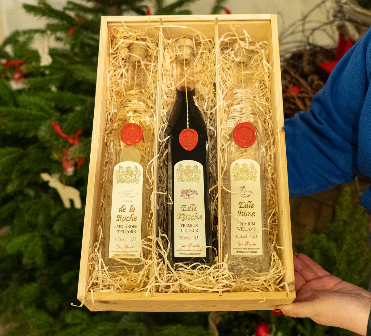 Premium Genuss-Set mit drei Likörflaschen in Holzkiste vor Weihnachtsbaum