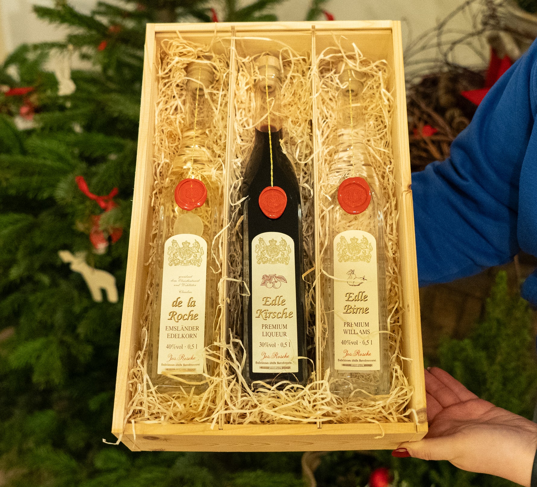 Premium Genuss-Set mit drei Likörflaschen in Holzkiste vor Weihnachtsbaum